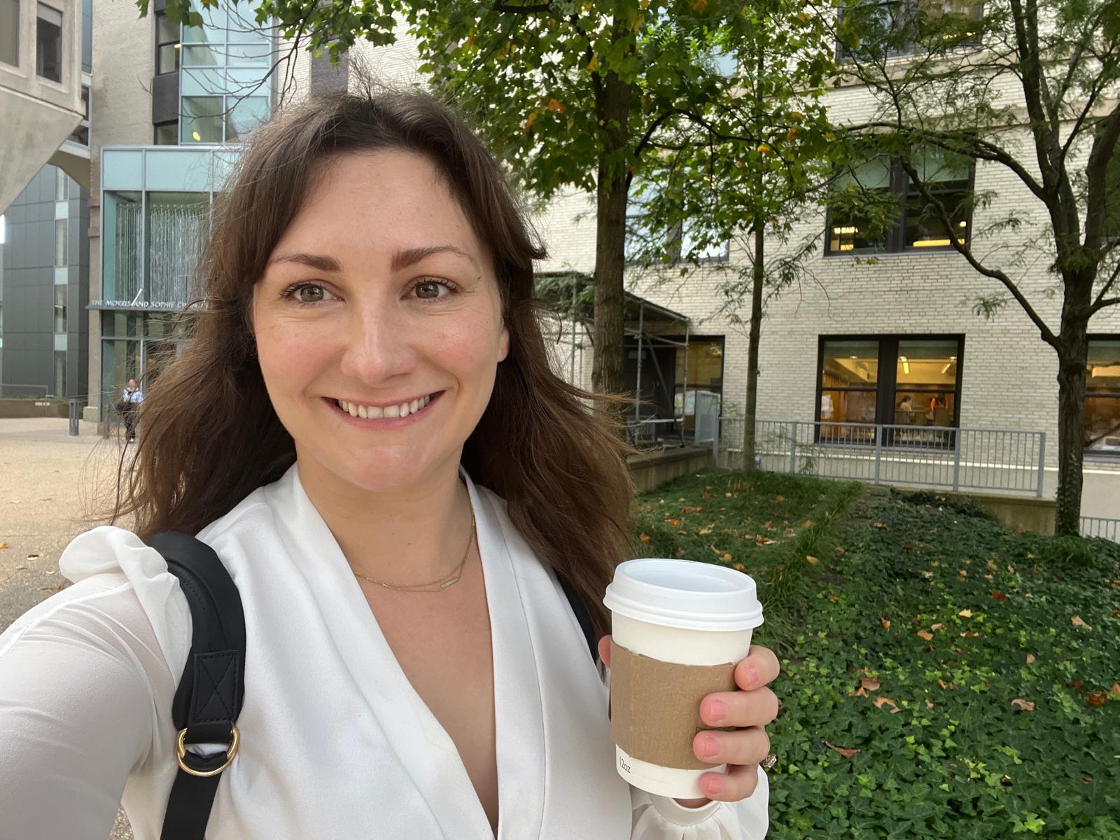 Chloe smiling outdoors with a coffee